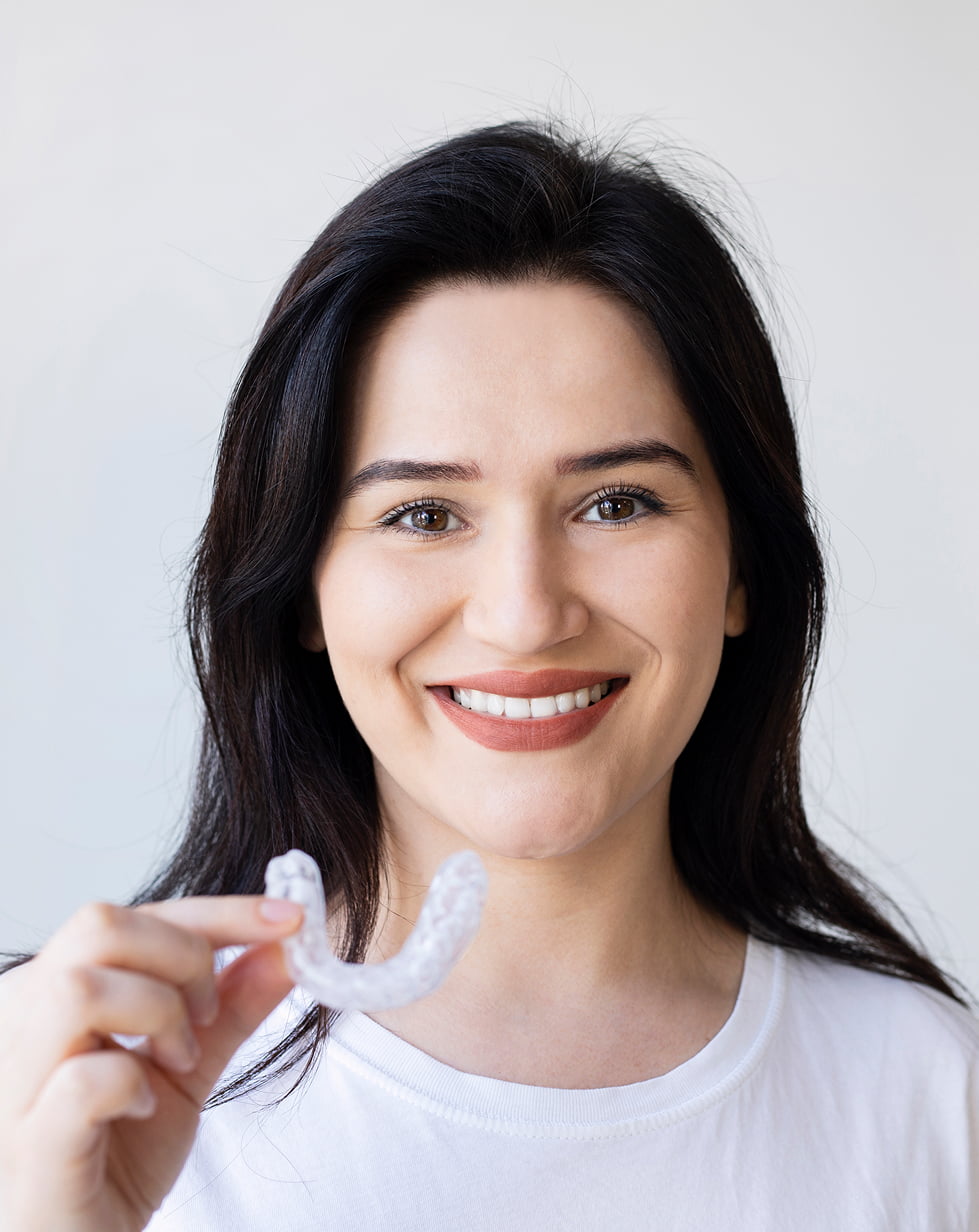 A woman smiles while holding a Invisalign, promoting dental hygiene and a positive attitude towards oral care