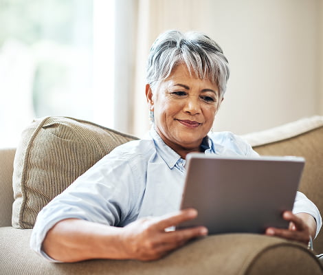 An older woman sitting on a couch, focused on using a tablet in a cozy living room setting