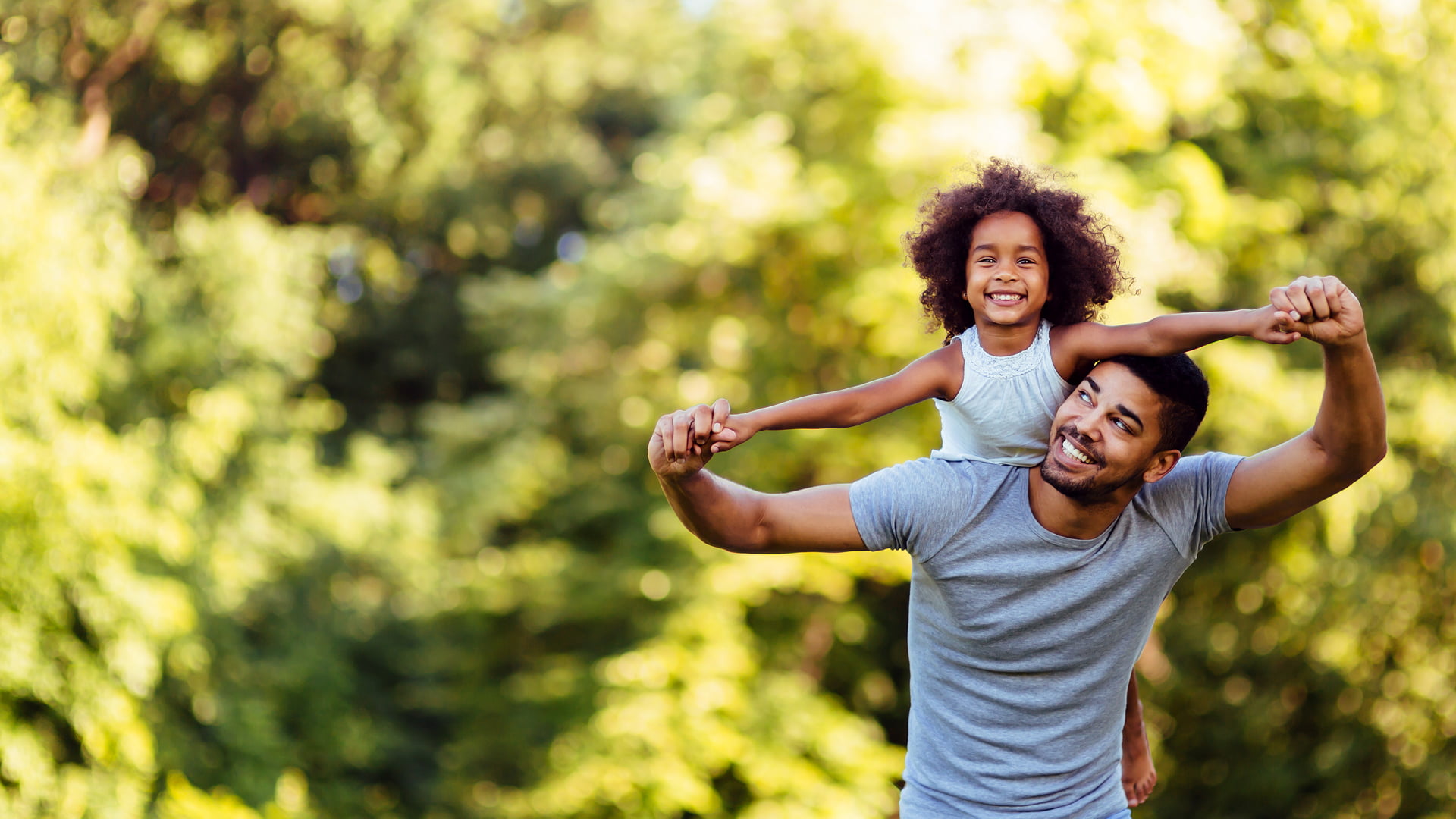 A man and a child joyfully playing together in a sunny park, surrounded by green grass and trees